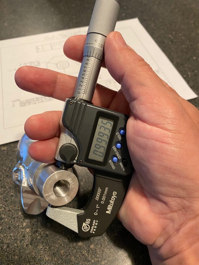 A micrometer is nested in the operator's hand with the thumb and index finger on the thimble.