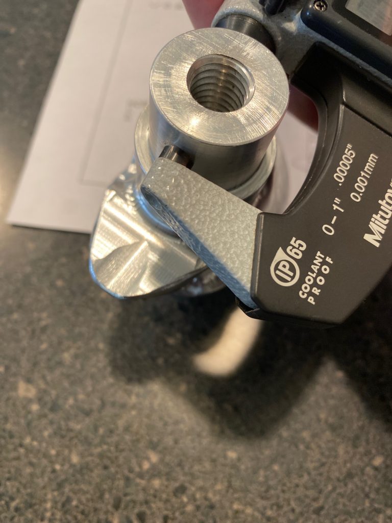 A close up picture of the flat micrometer anvil resting against the round surface of a boss feature.