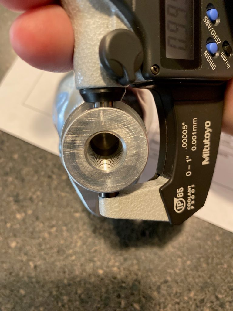 A close up picture of the flat micrometer anvil resting against the round surface of a boss feature.