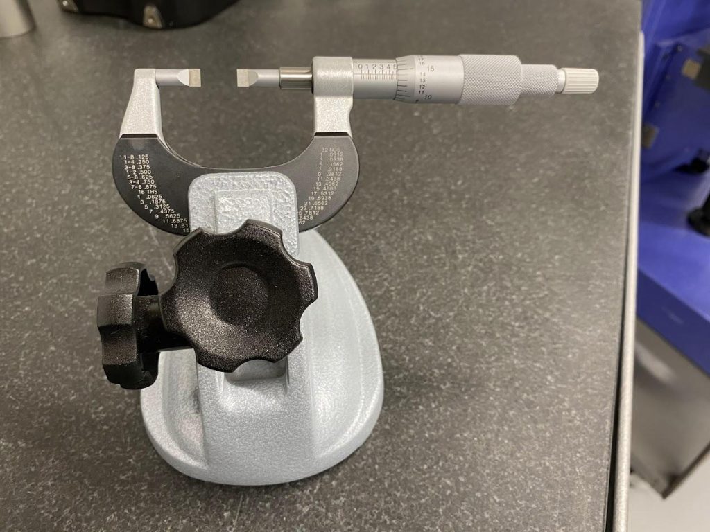 A blade micrometer placed in the jaws of a micrometer stand.