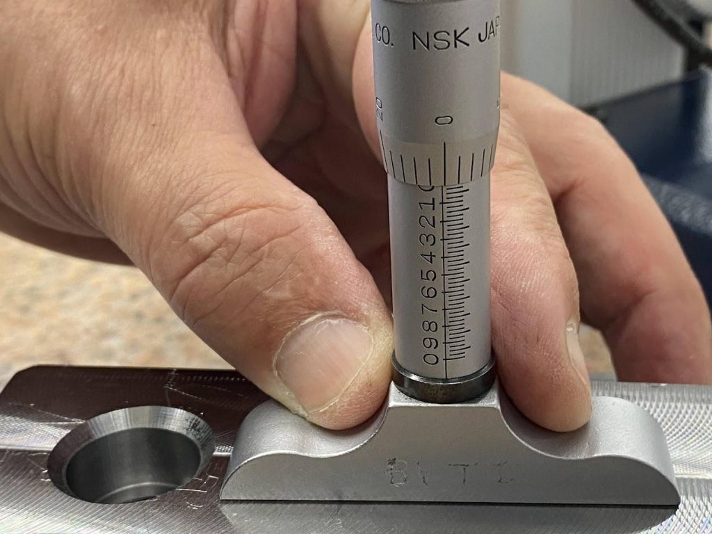 An operator is holding a depth mic on the top flat surface of a part and verifying the vernier scale indicates zero.
