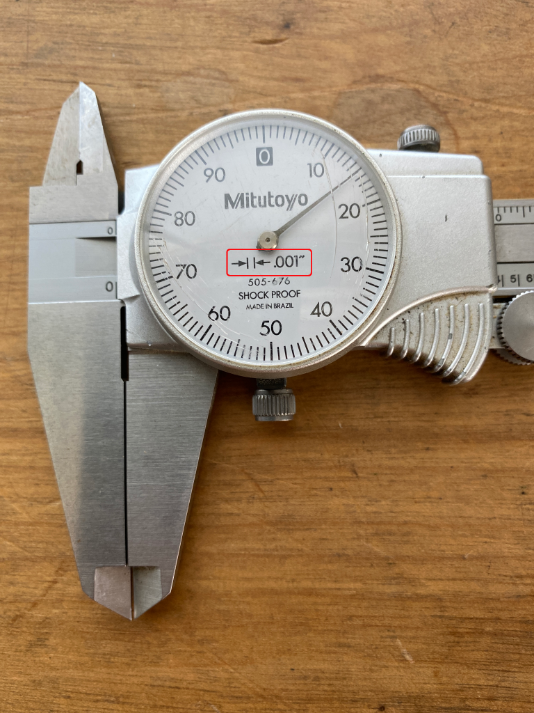 A dial caliper used to measure three decimal dimensions has a legend in the bezel explaining that every mark equals .001”.