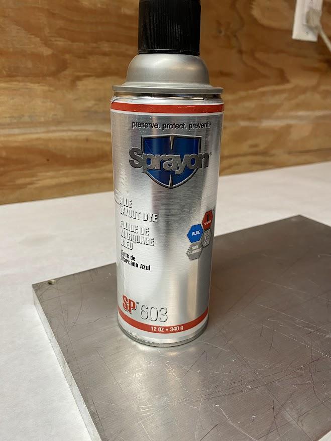 A spray can labeled as layout dye is resting on a piece of aluminum plate.