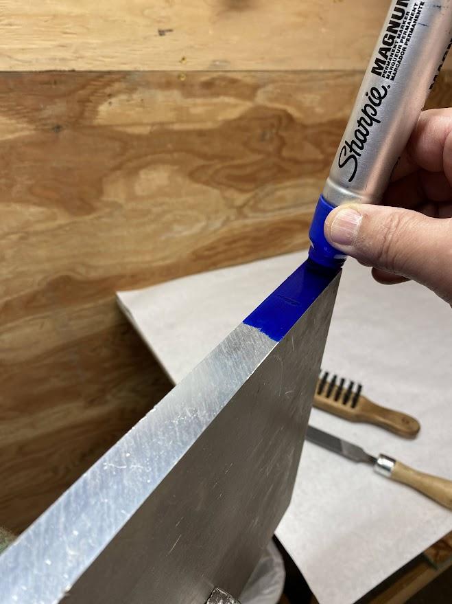 A permanent marker applying blue ink to the edge of aluminum stock.