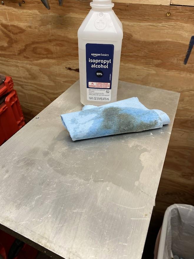 A bottle of isopropyl alcohol and a damp rag resting on a cleaned aluminum plate.