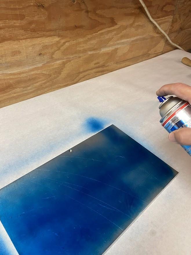 An aluminum plate being sprayed with blue layout dye.