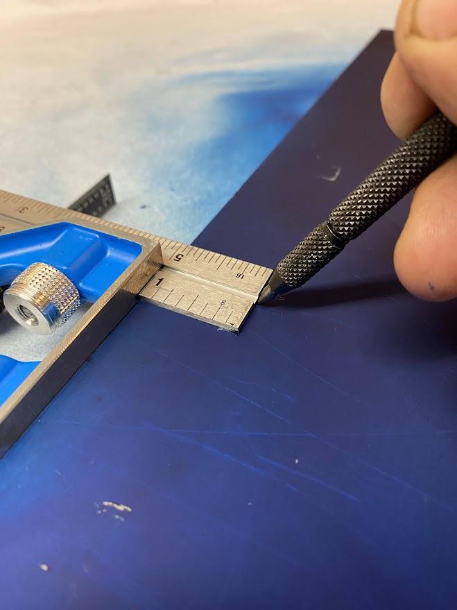 A combination square and a scribe are used to create a layout line parallel to the edge of the stock.