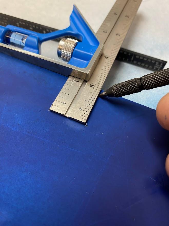 A perpendicular line is scribed by using a combination square to reference the edge of the stock.