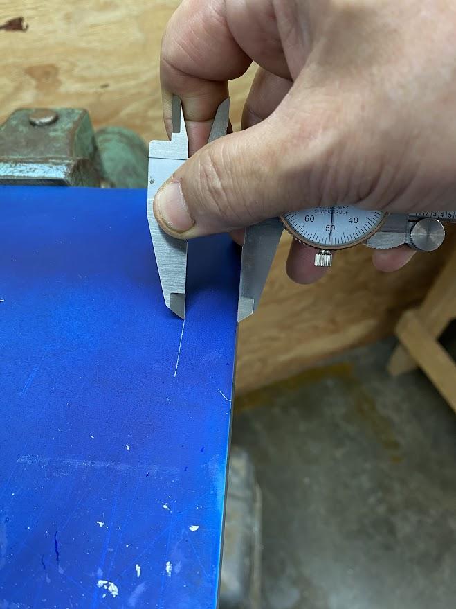 An operator dragging the slide caliper along the edge of the stock and scribing a line in the layout dye.