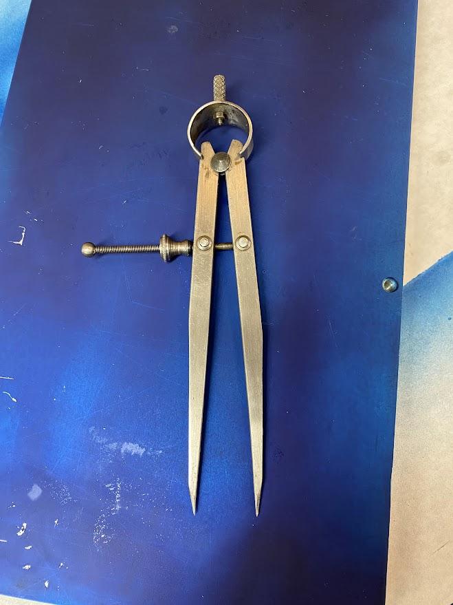 A layout caliper has two legs with points connected at one end and held apart with an adjustment screw.