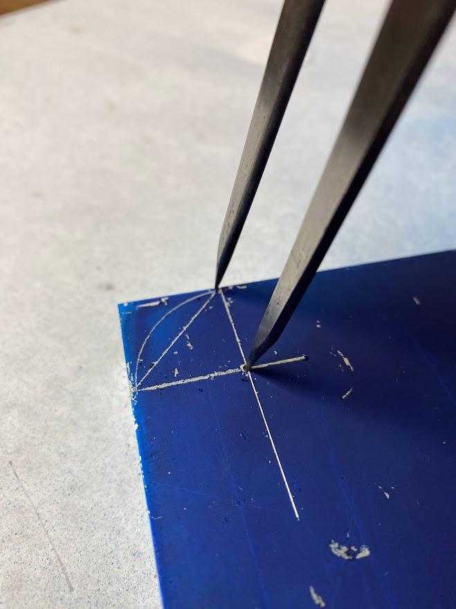 A divider point placed in a punch indent scribing an arc with the other point.