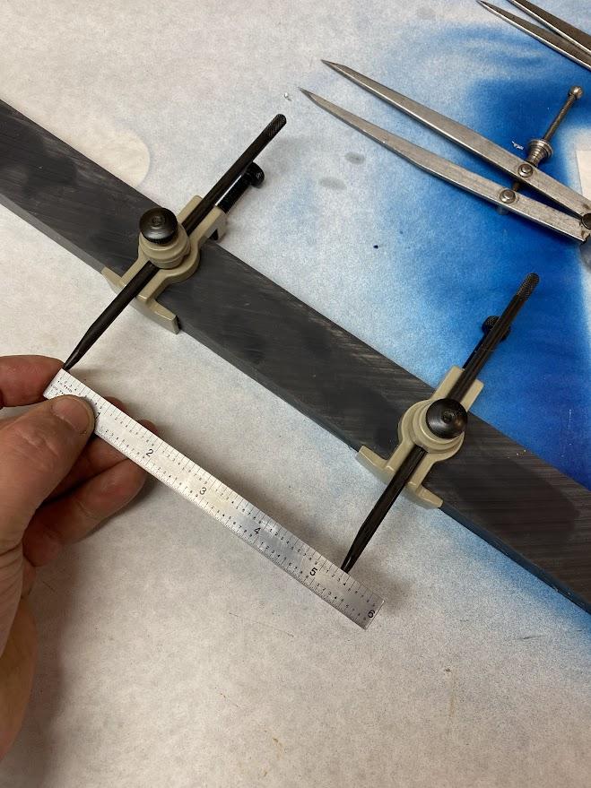 A worker is setting the trammel's points using a ruler.