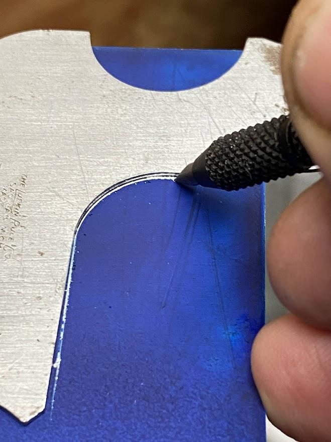 A radius gage blade placed on a part that has layout dye applied and a scribe applying an arc along the edge of the radius gage.