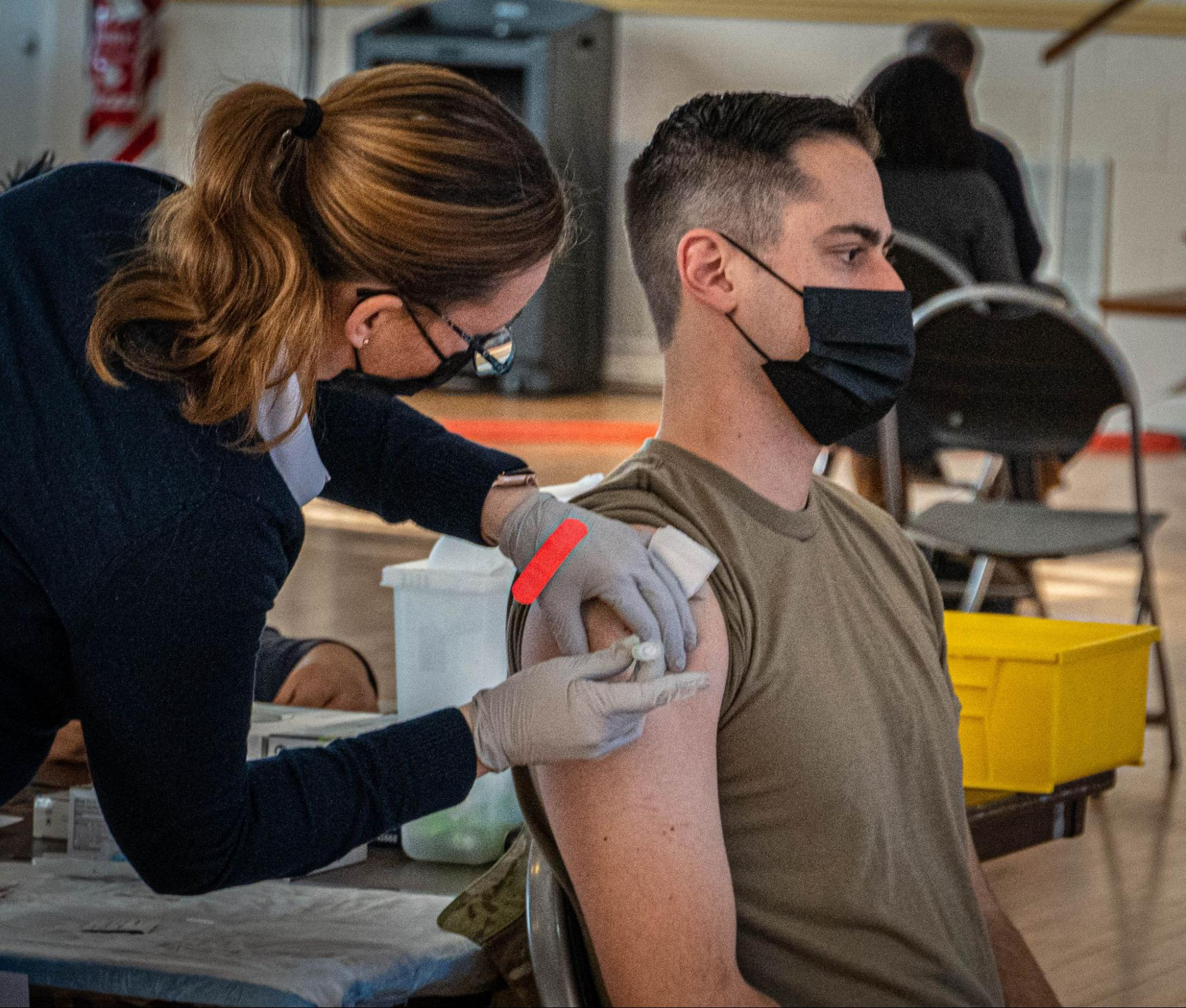 A male sitting in a chair receiving a vaccine in his arm.