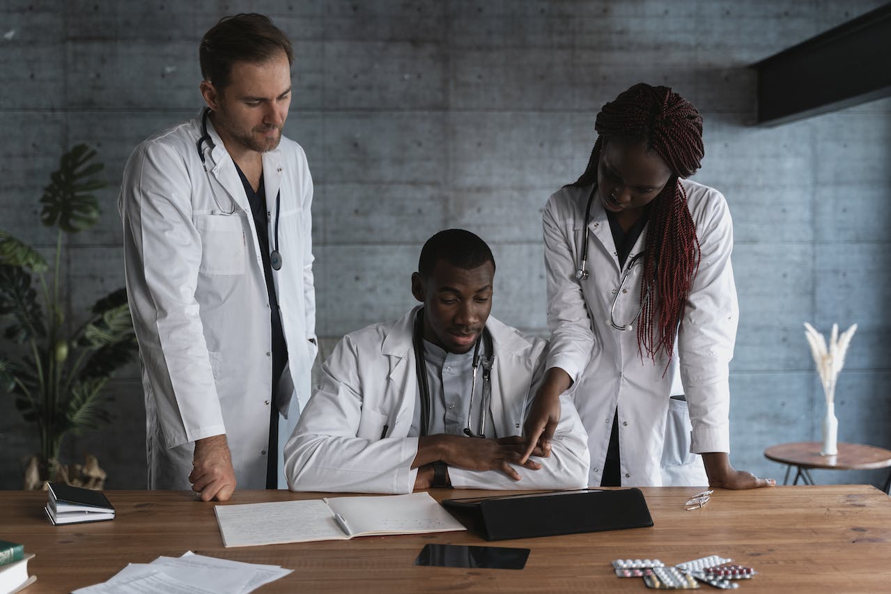 3 healthcare professionals huddled around a wooden table discussing patient information