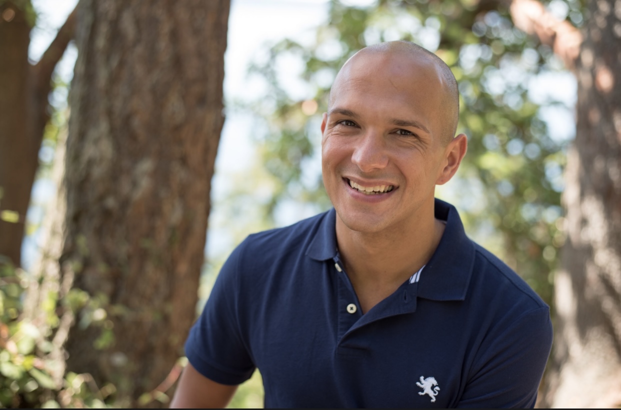 Brandon Censon sitting in a sunny stand of trees smiling