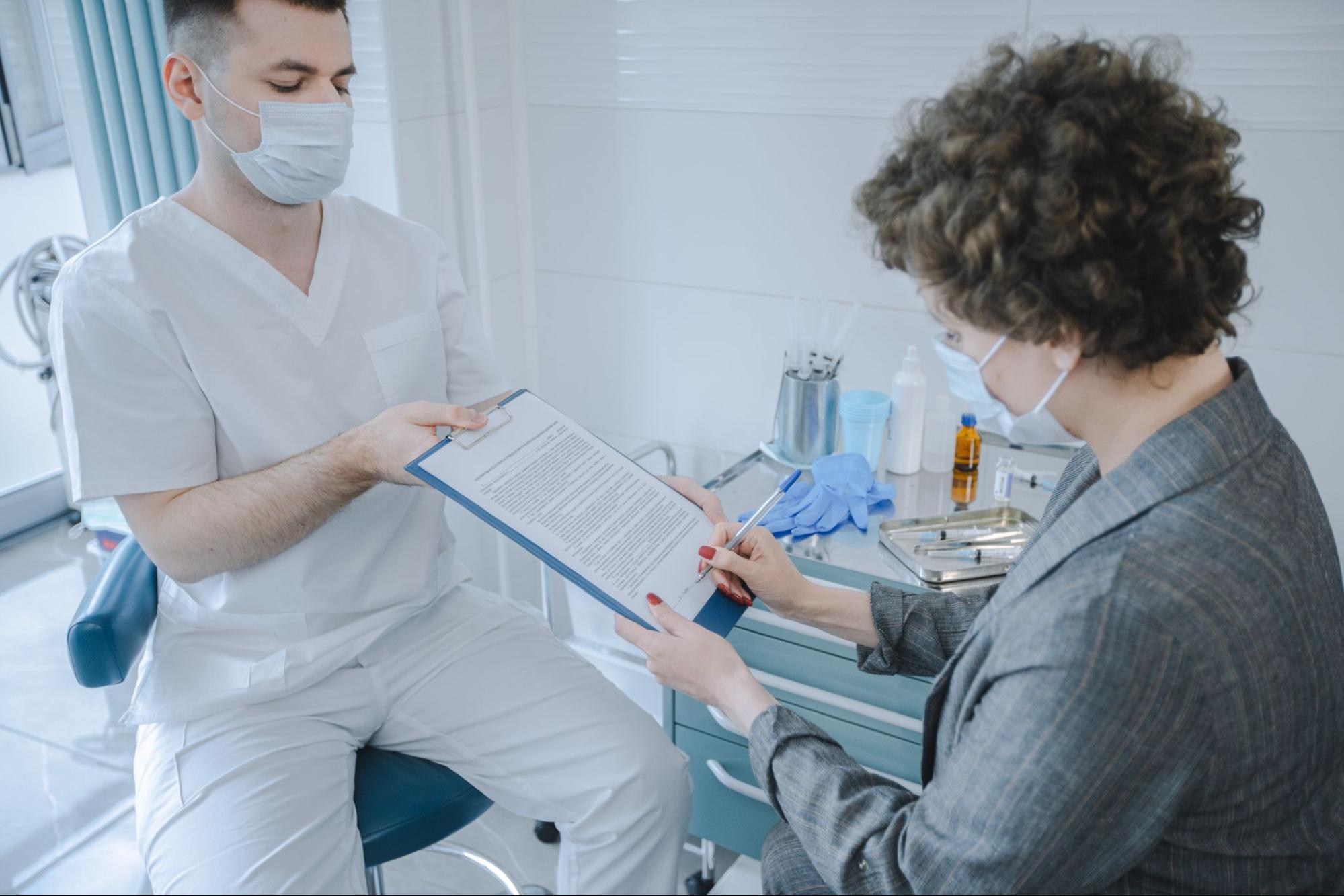 A man wearing scrubs provides a woman with a consent form to sign