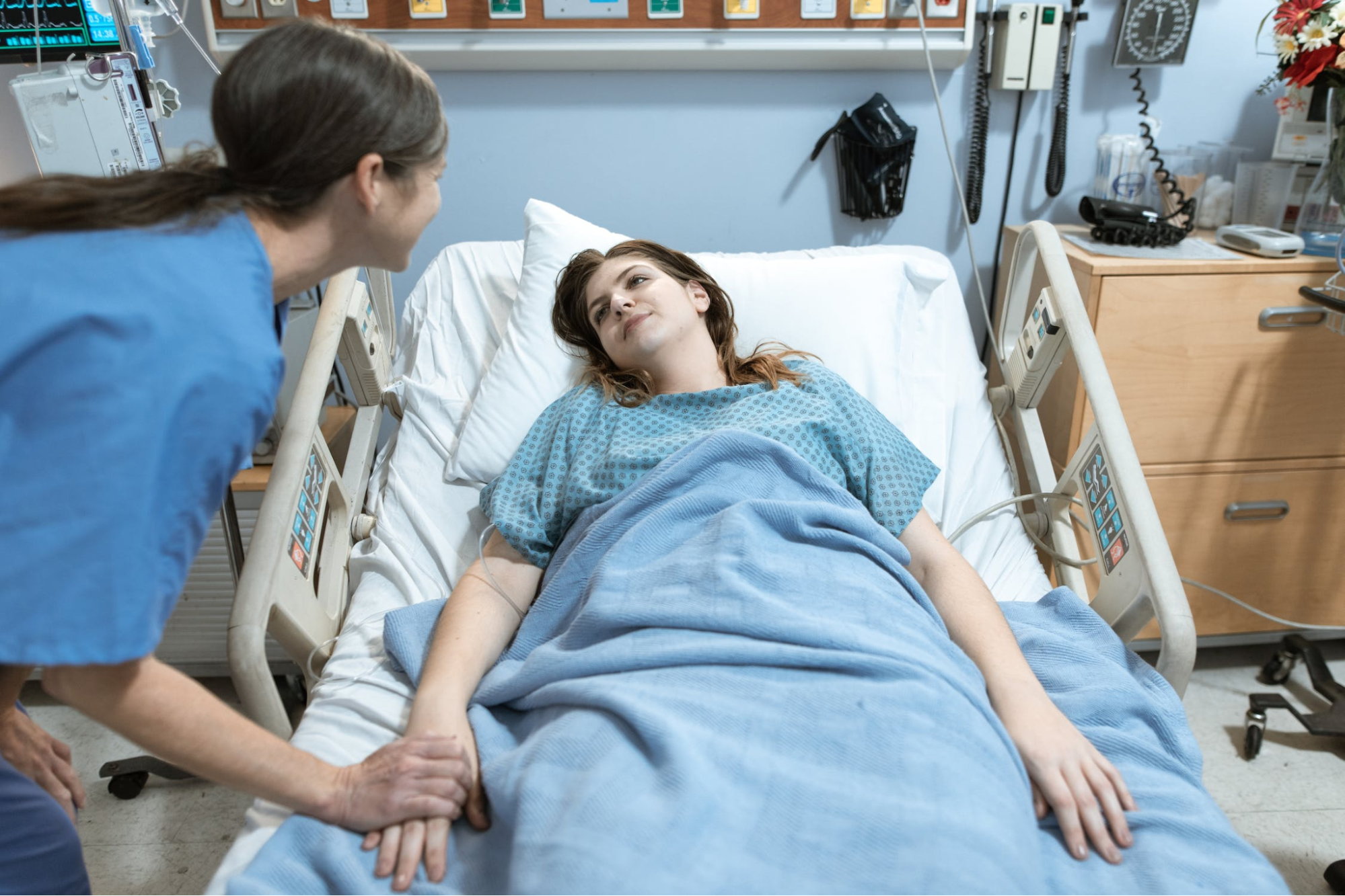 Nurse standing over a patient’s bed holding the patient’s hand