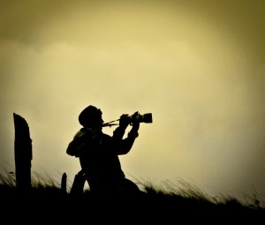 A photographer kneeling in a field with a dusty sunset