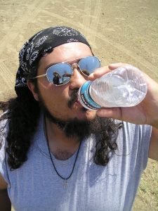 a man wearing sunglasses drinking from a water bottle in a hot environment