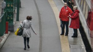 a woman walking along a platform carrying her bags while workers in uniform converse on the side