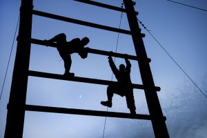 two soldiers are silhouetted in twilight scaling a giant ladder on an obstacle course