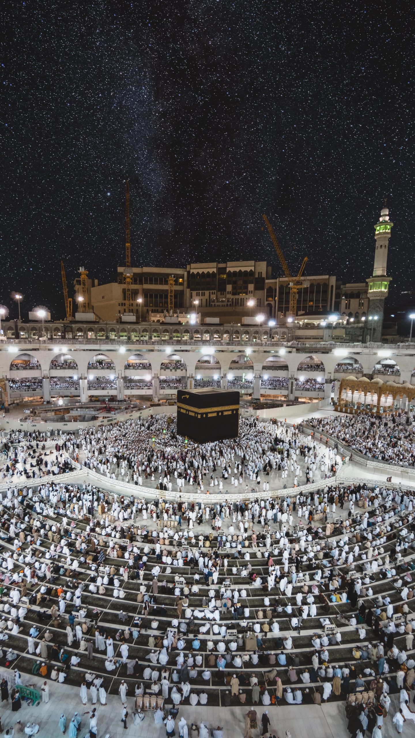 The night sky over worshippers surrounding a black cube-shaped building in a large courtyard.