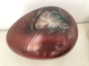 A smooth ovular stone, in deep red with black cracks running along its surface. The surface is a muddied silver where the cracks are widest.