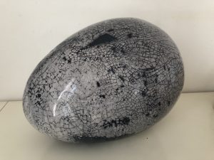 A smooth ovular stone, in gray with many small black cracks running along its surface. There are three large black splotches across the surface.
