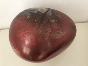 A smooth ovular stone, in deep red with a black crack on the top. The surface is a muddied silver near the crack on the upper left.