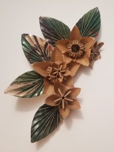 A series of three tan paper flowers and five green leaves. They are arranged in a half circle.