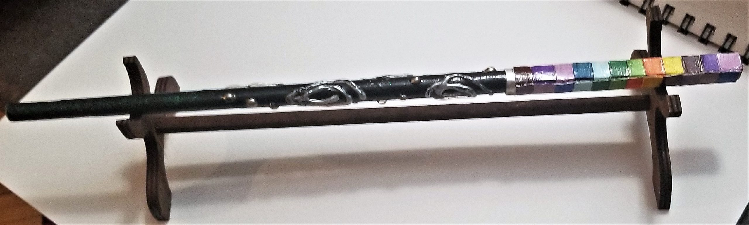 A black wand with swirls and dots of silver. The handle is has squares of several colors in a repeating pattern.