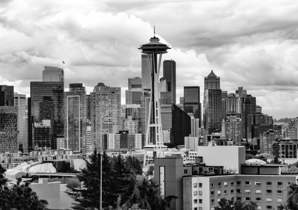 The Seattle skyline is rendered in grayscale, the Space Needle prominently displayed in front of tall buildings. Smaller buildings and some trees line the bottom.