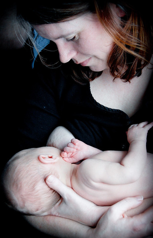 A light-skinned mother cradles a young infant in her arms, and the baby is breastfeeding.