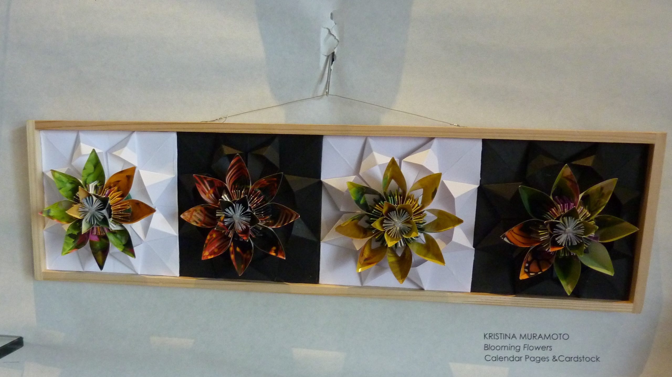 Four folded paper flowers in a variety of colors mounted on a wooden tray