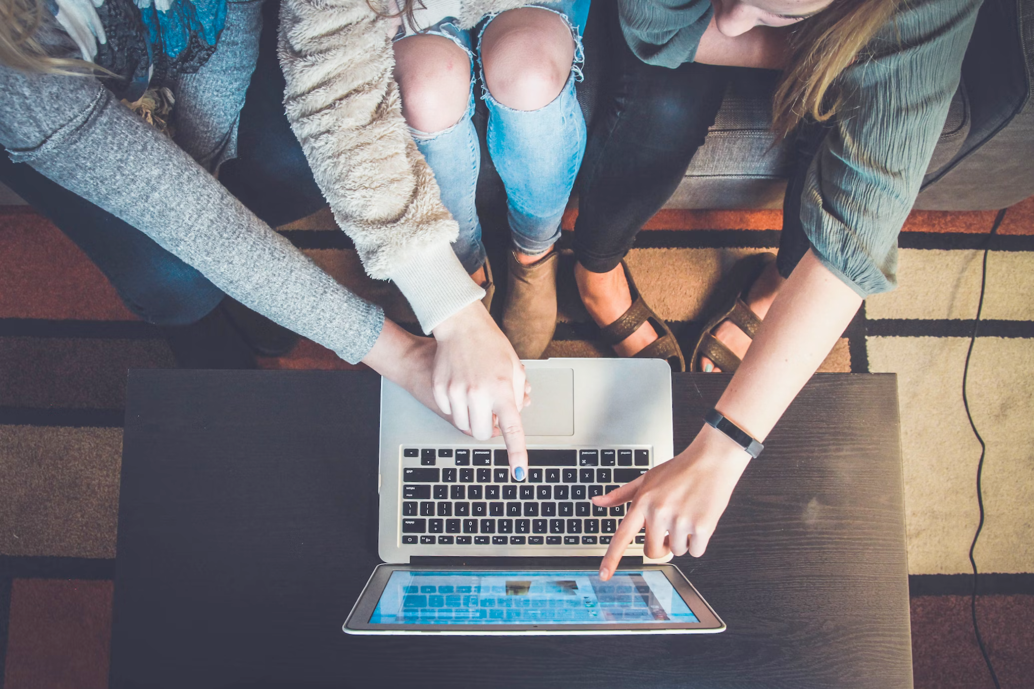 Three people sitting together looking at a computer together pointing to the screen and keyboard.