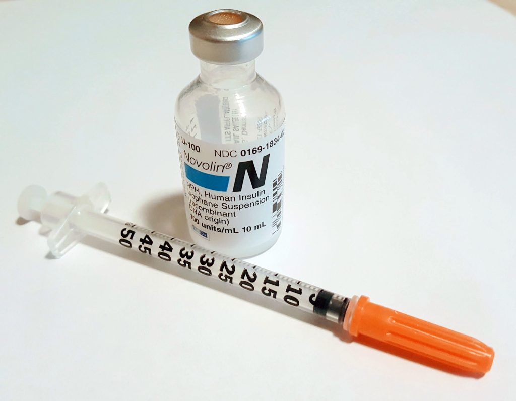 Photo showing closeup of a vial of N P H insulin and a capped syringe