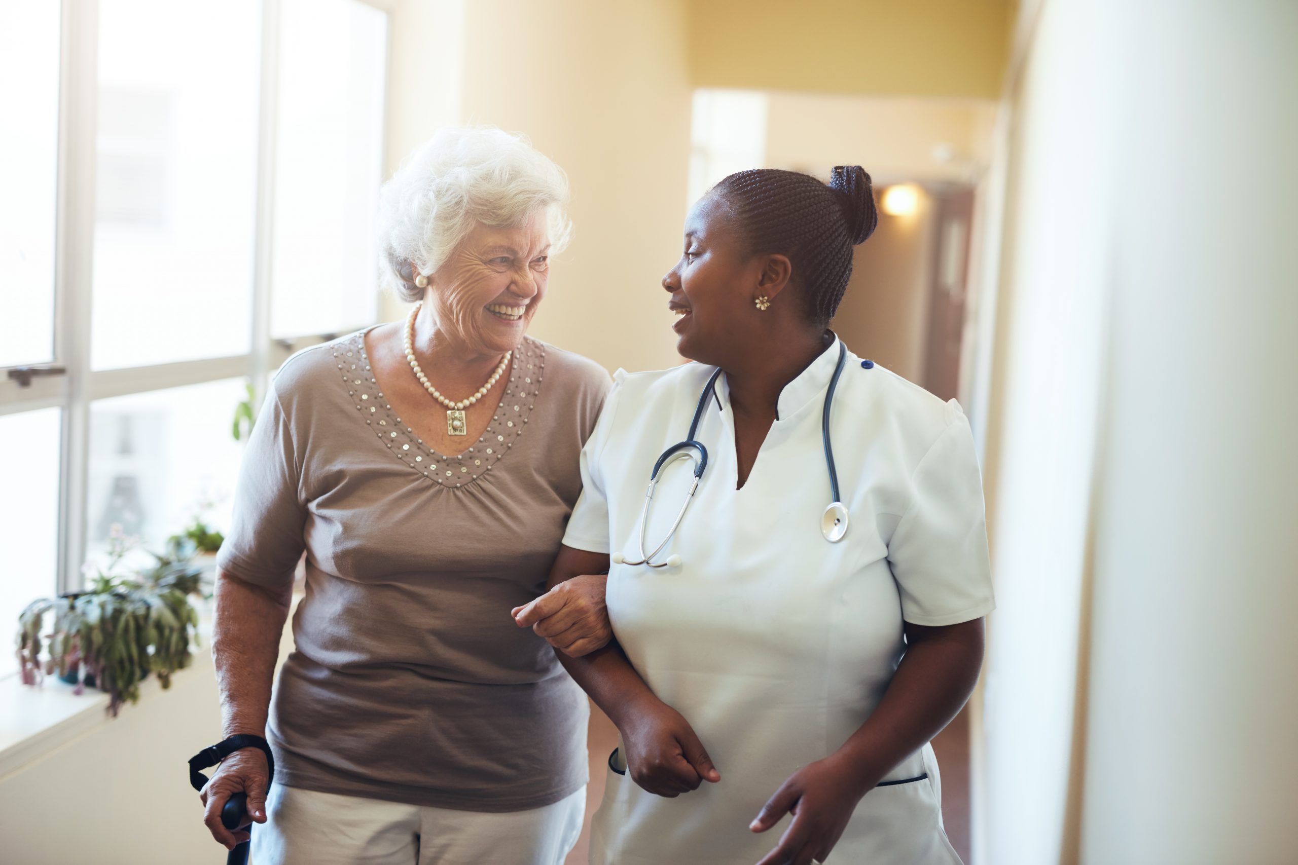 Image of an elderly woman and a nurse, walking together, smiling at each other