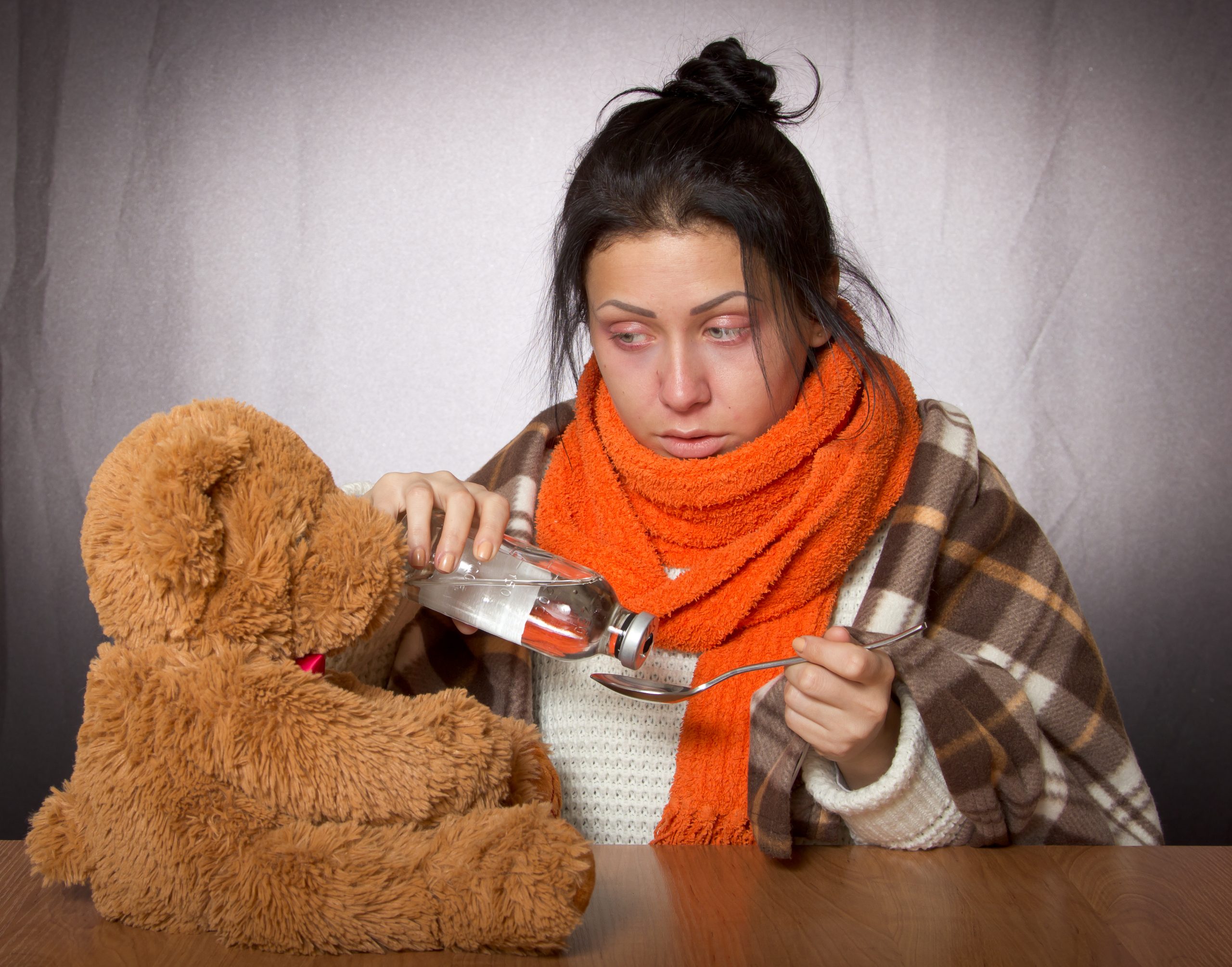 Image person pouring simulated medicine into a spoon while looking at a teddy bear