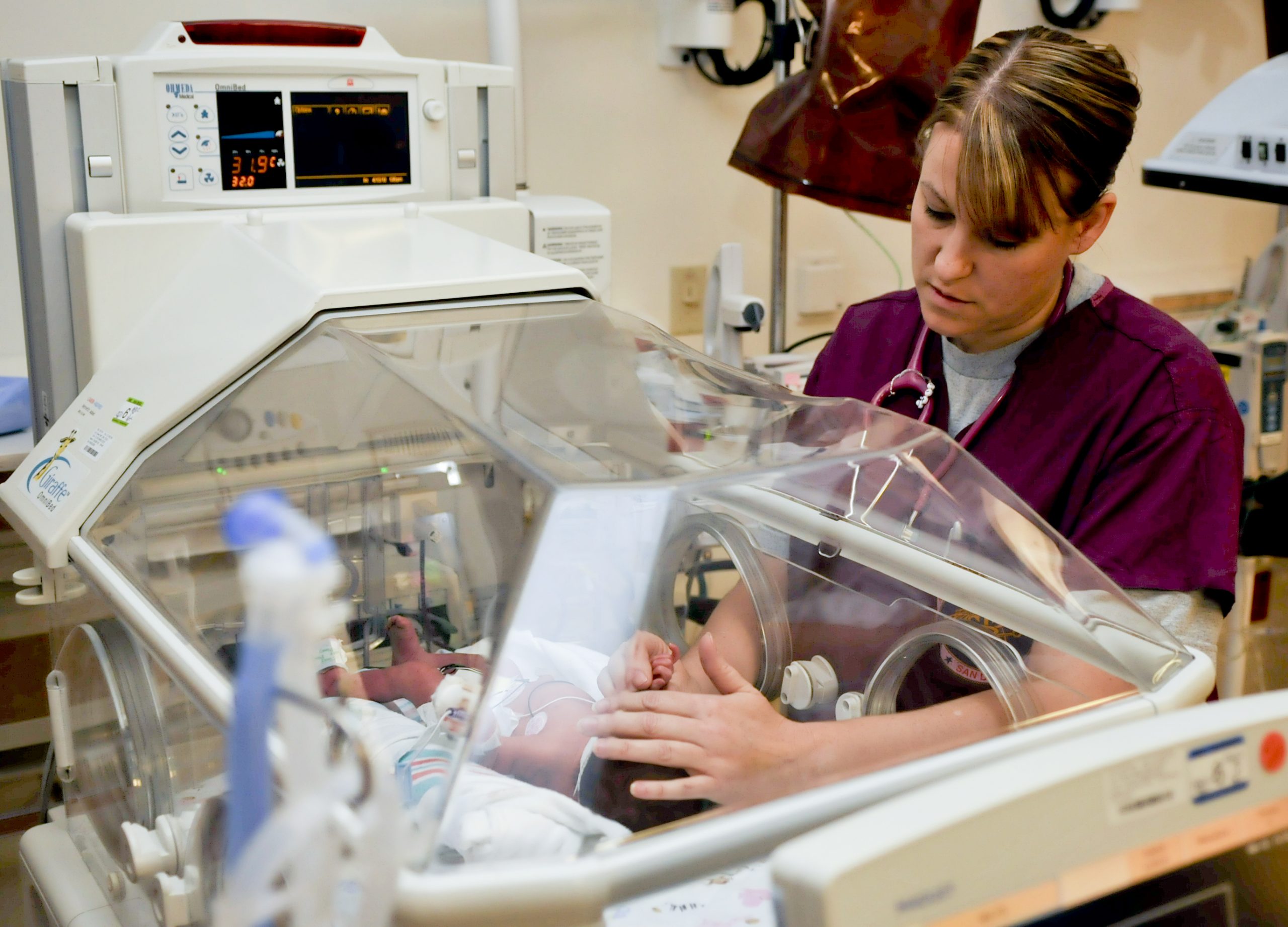 Photo showing nurse touching infant in incubator