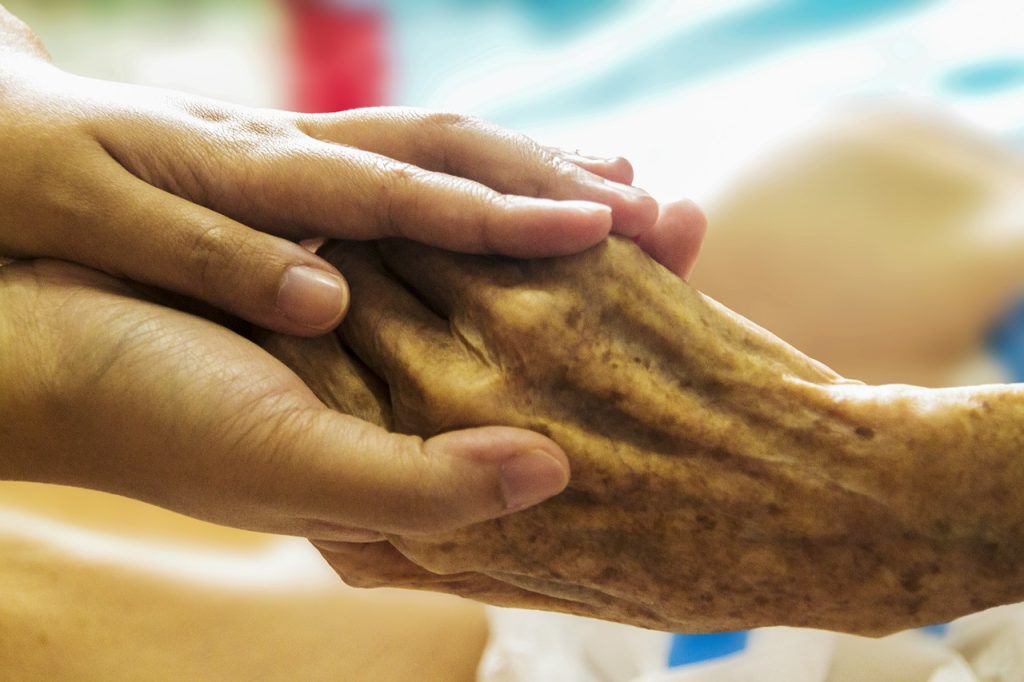 Photo showing closeup of a younger hand holding an elderly one